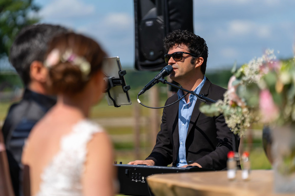 Hochzeitssänger Eugen Nevo singt und spielt Klavier bei einer sonnigen Trauung im Freien und trägt dabei eine Sonnenbrille